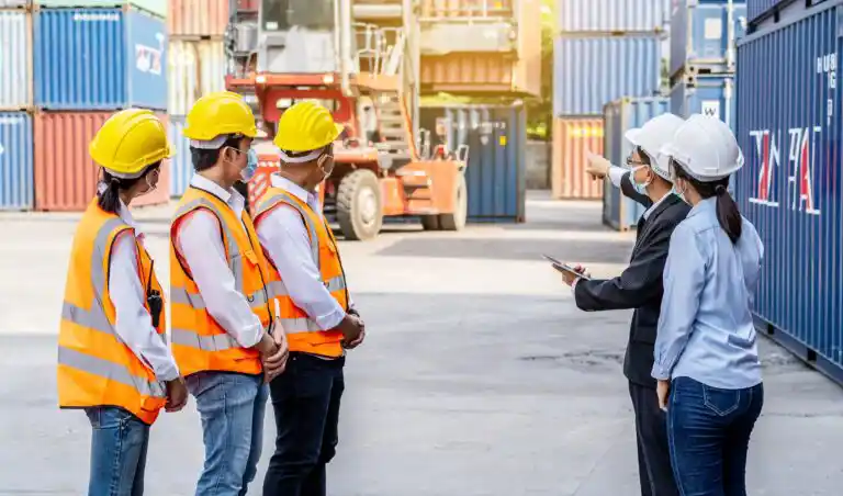 Management team points towards heavy equipment that requires safety training, while portside dock staff considers.